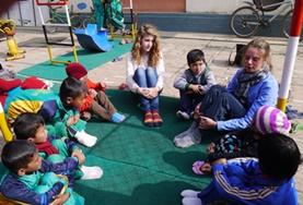 Volunteer Nepal Two Care & Community volunteers in Nepal sit in a circle with local children, preparing to play an educational game.