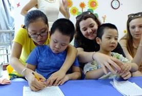 Volunteer Care Childcare volunteers work closely with children from a kindergarten in China, helping them to draw and colour in.