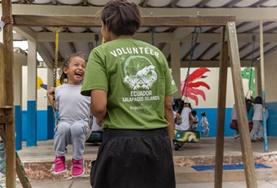 Volunteer Care A childcare volunteer pushes a young girl on a swing in a playground in Ecuador.