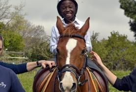 Volunteer Care A volunteer supports a disabled boy as he rides his therapy horse at our Equine Therapy placement in South Africa.