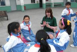 Volunteer Care A high school volunteer sits in a playground in China with local children, playing an educational game with them.