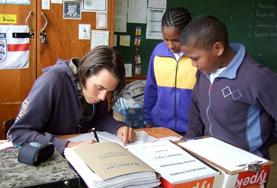 Volunteer Teaching Two school children watch as a Teaching volunteer demonstrates how to complete the English homework assigned to them.